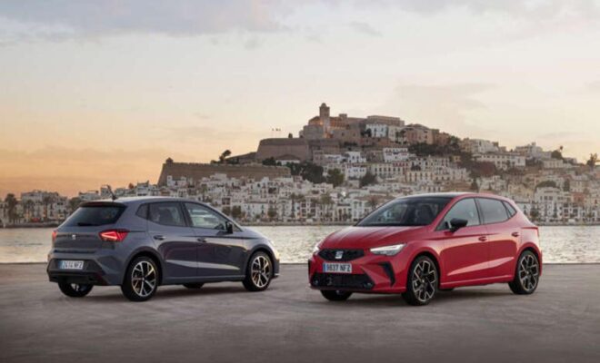 Two sporty compact cars parked with a historic town in the background at sunset.
