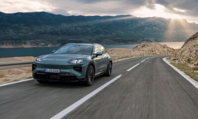 A sleek electric car driving on a mountainous road under a cloudy sky.