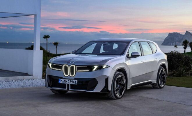 A sleek silver BMW iX electric SUV parked at sunset with palm trees in the background.
