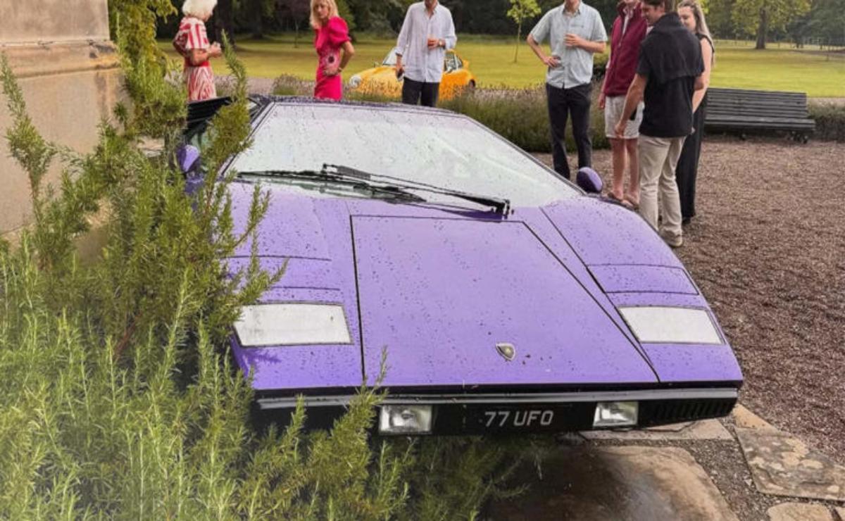 A purple sports car partially submerged in water with people observing.
