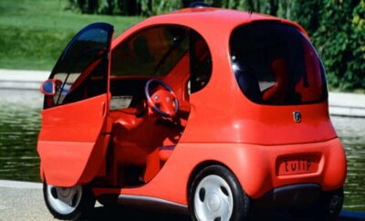 A small, bright red compact car with its door open on a sunny day.