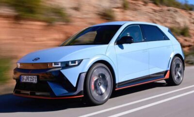 A sleek blue electric car driving on a road with rocky background.