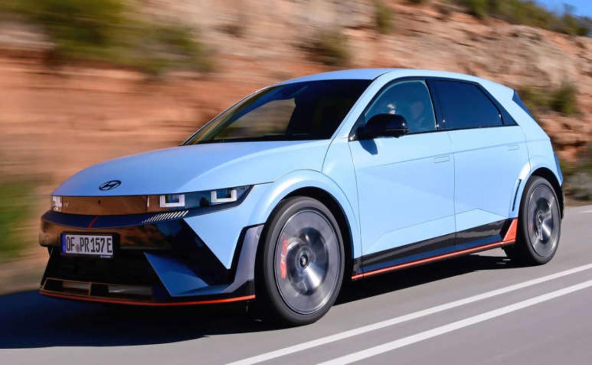 A sleek blue electric car driving on a road with rocky background.