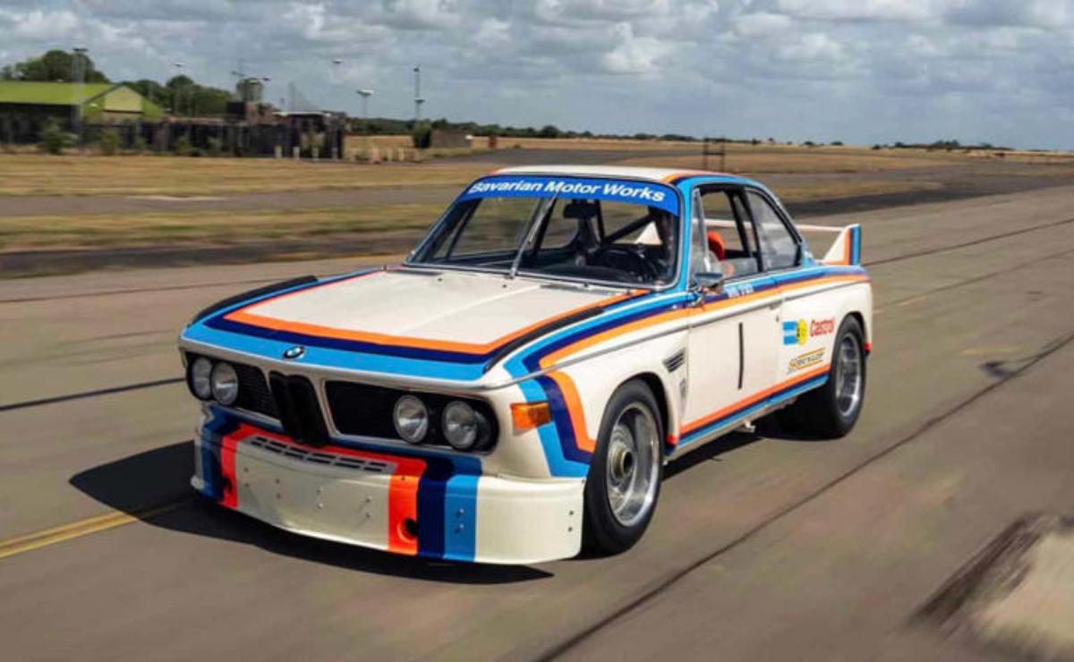 Classic BMW race car with iconic Martini livery on a racetrack.