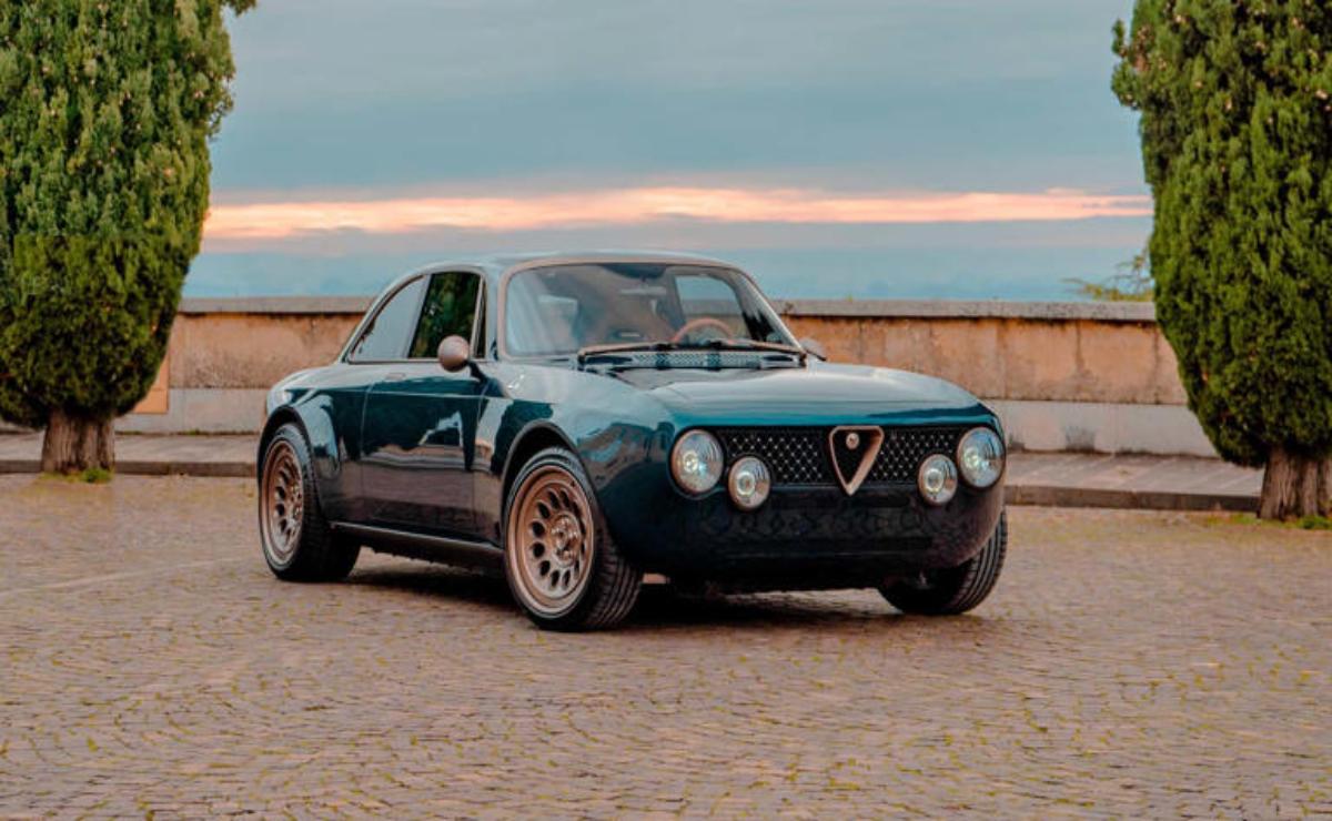 Classic black Alfa Romeo car parked on cobblestone at sunset.