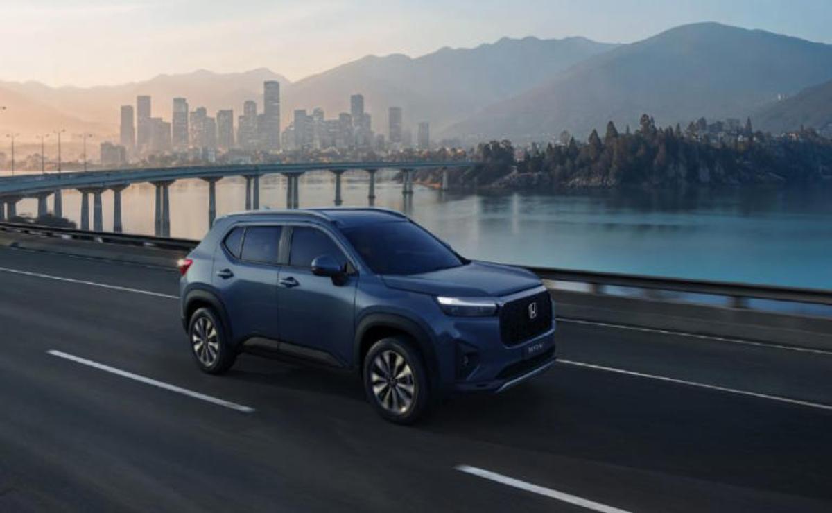 A sleek blue SUV driving on a highway with a city and mountains in the background.