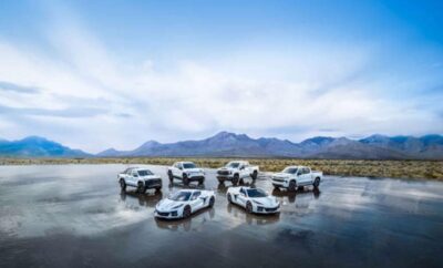 Seven white SUVs and cars parked on a reflective wet surface with mountains in the background.