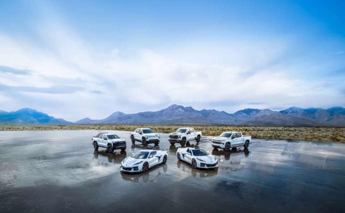 Seven white SUVs and cars parked on a reflective wet surface with mountains in the background.