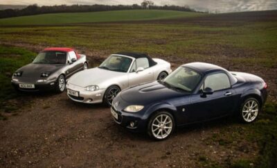A lineup of three Mazda MX-5 Miata cars parked on a dirt path near a field.