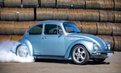 A classic blue Volkswagen Beetle parked in front of stacked hay bales.