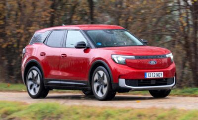 Red electric SUV driving on a road with autumn trees in the background.