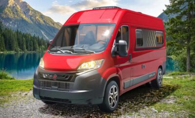 Red camper van parked on a gravel path with mountains in the background.