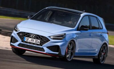 Blue Hyundai hatchback driving on a road with sporty design.