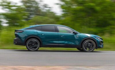 A teal electric SUV driving on a road surrounded by greenery.