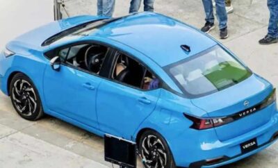 A blue car with a person inside and people standing nearby.