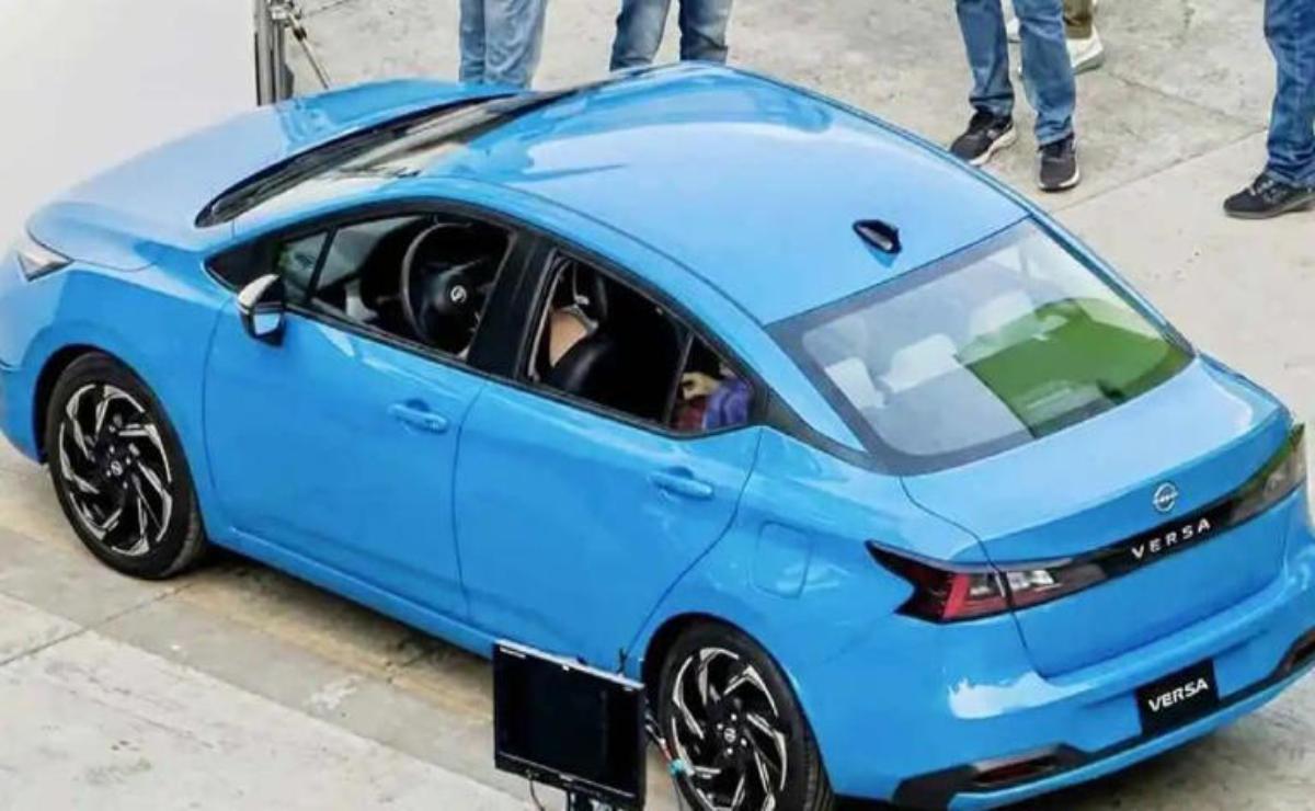 A blue car with a person inside and people standing nearby.