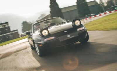 Classic black convertible sports car driving on a racetrack.