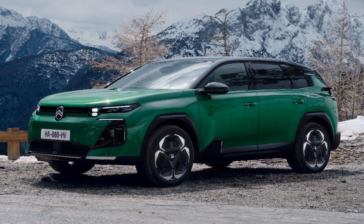 Green modern SUV parked in mountainous terrain with cloudy sky.