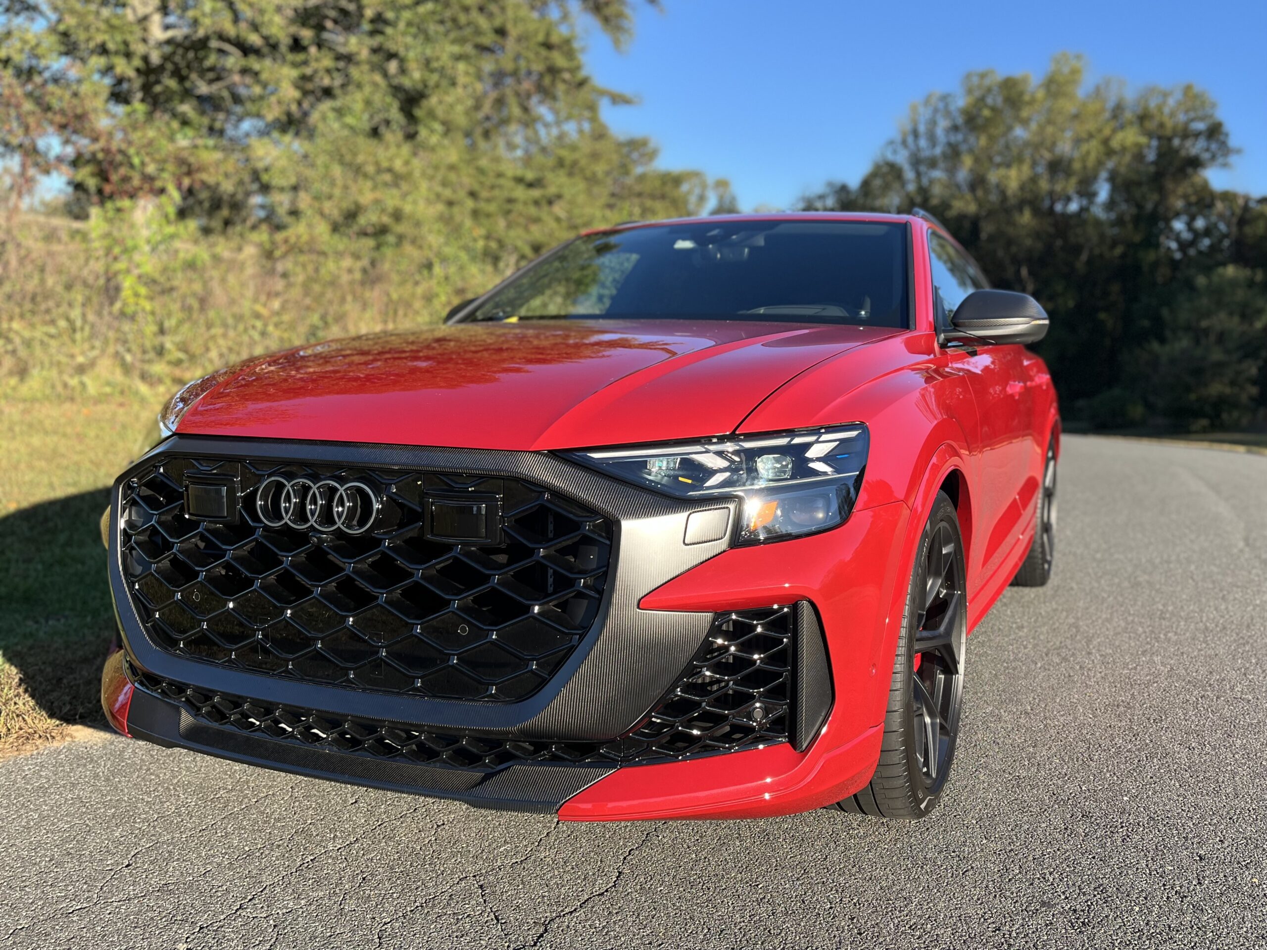 Red Audi SUV parked on a sunny road with greenery.